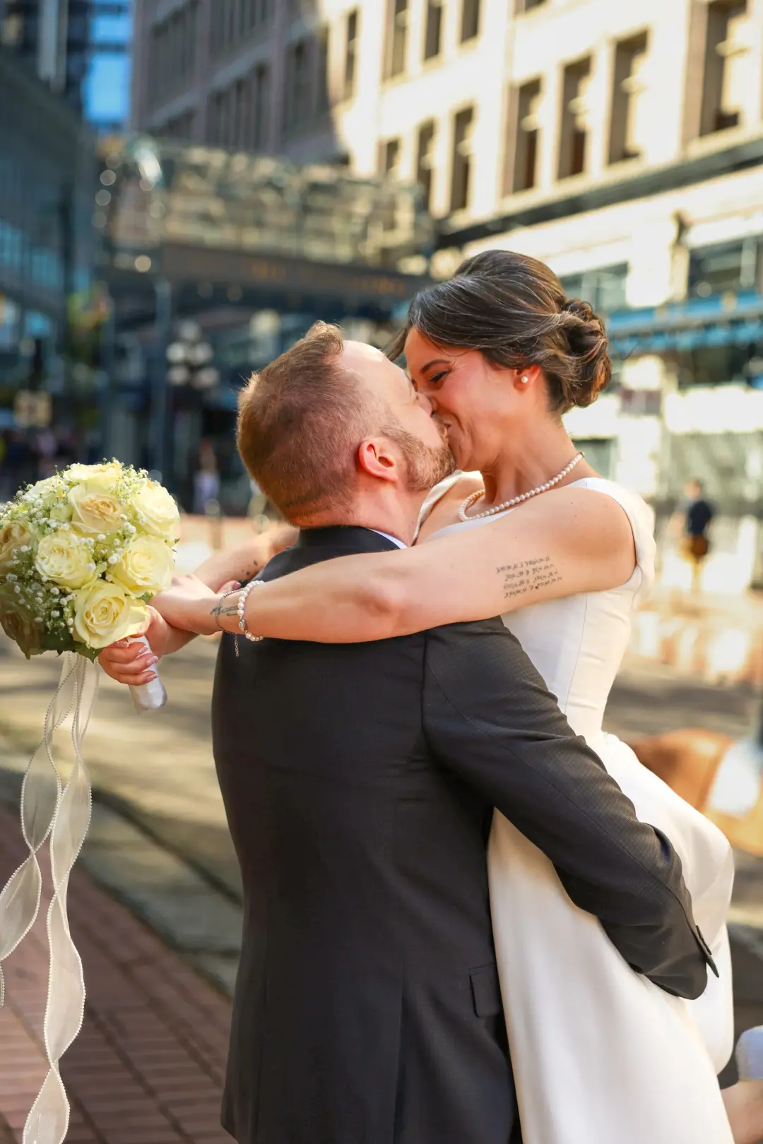 A groom lifting his laughing bride for a kiss on a sunny downtown street.